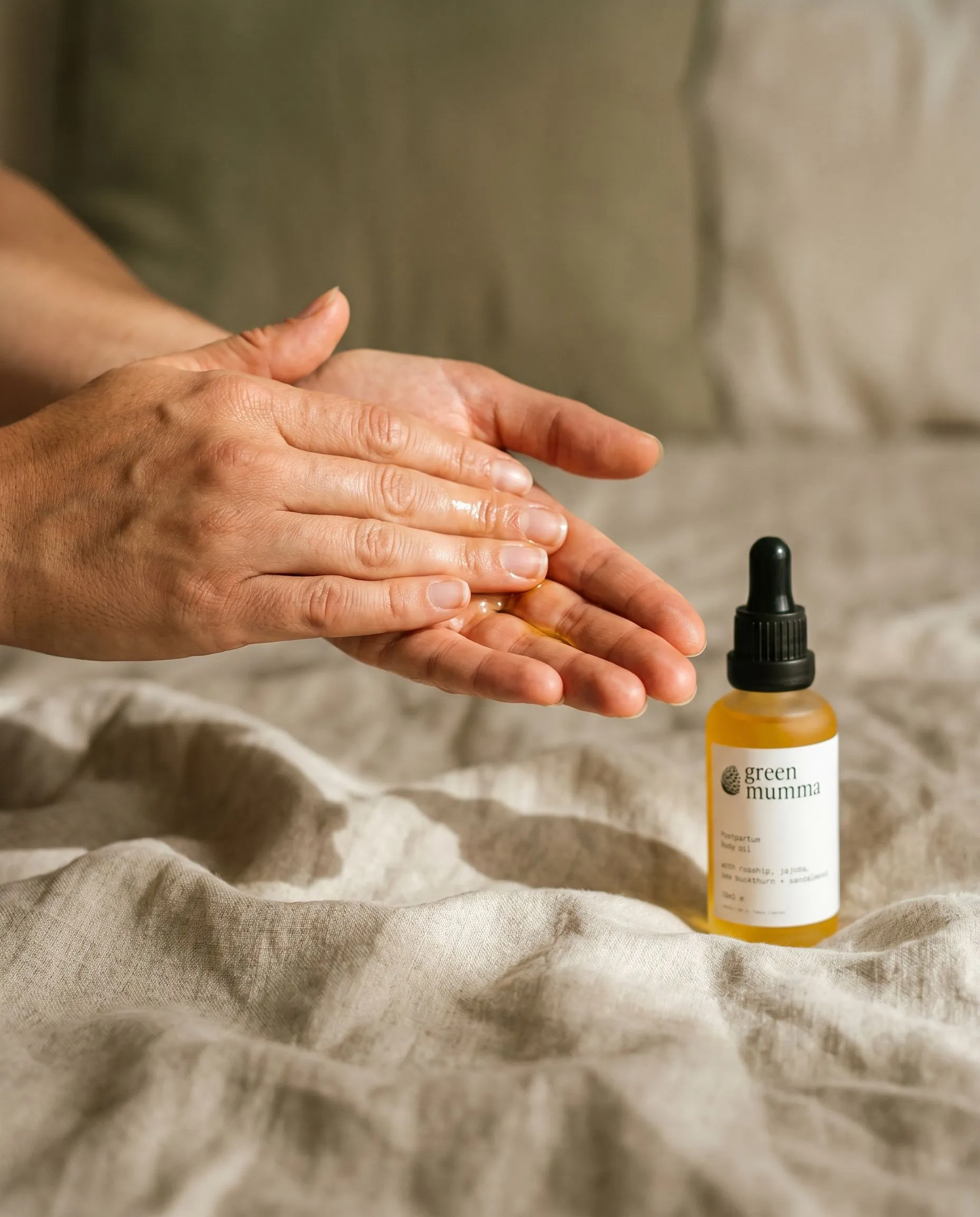 Hands pressing Green Mumma body oil together over linen